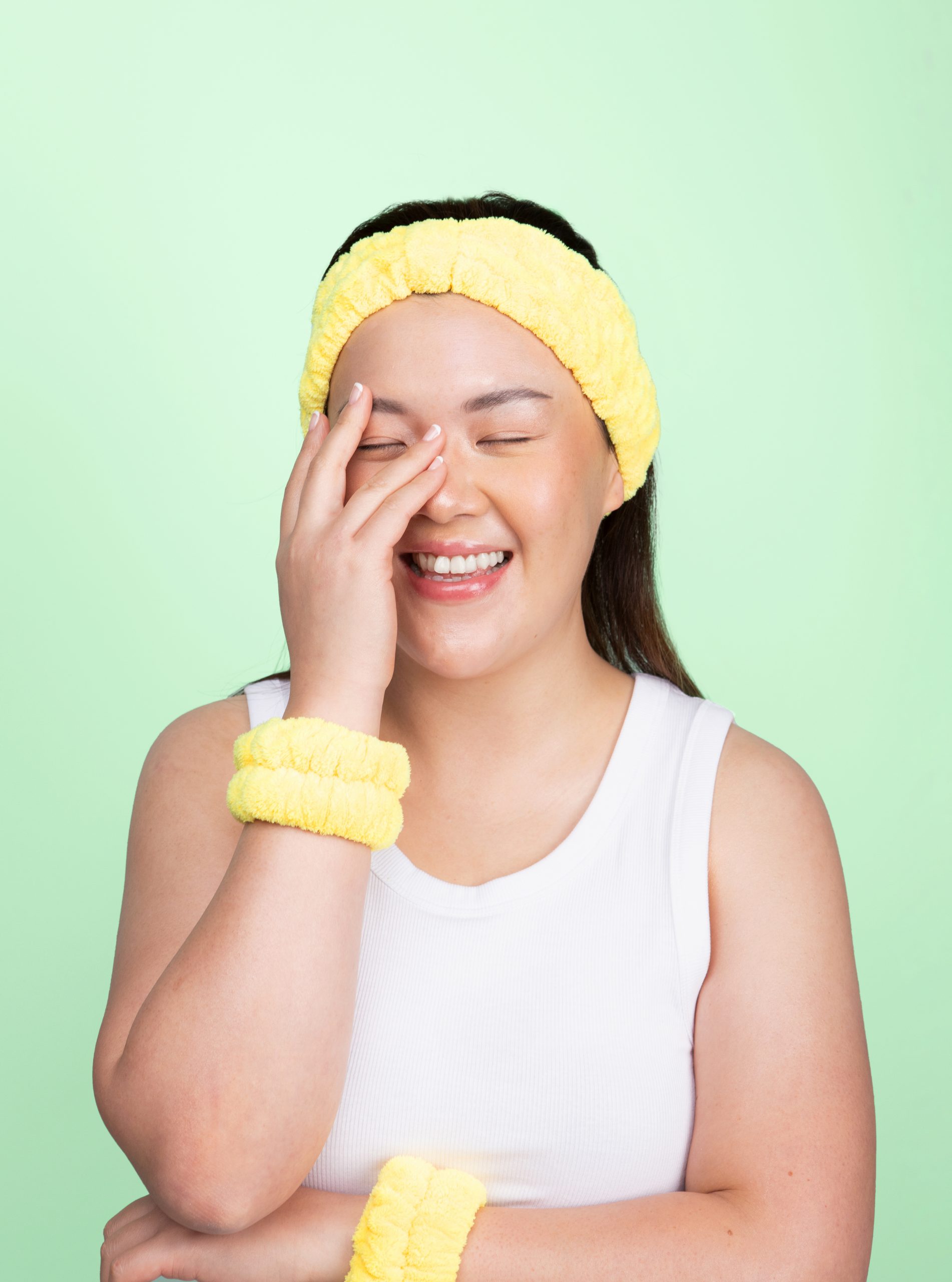 Girl laughing wearing yellow skincare headband in turban style and matching yellow spa wristbands