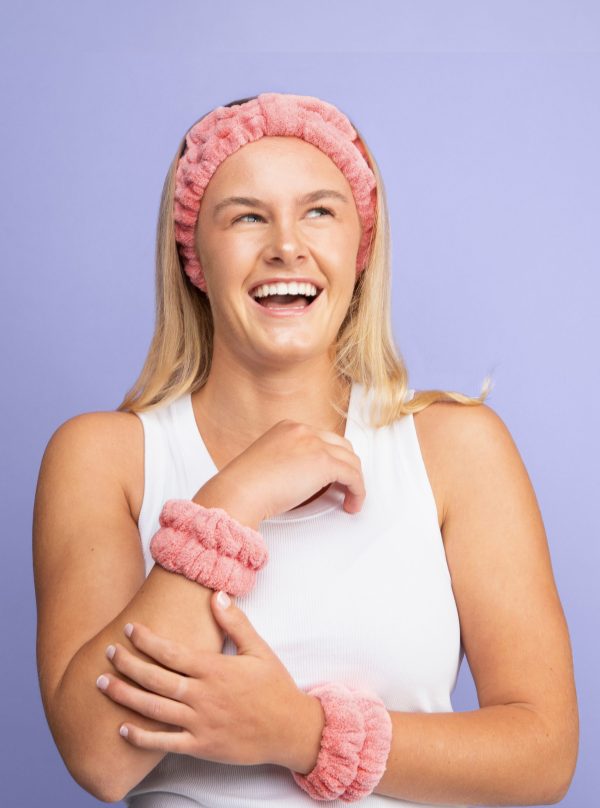 Girl laughing wearing pink skincare headband in turban style and matching pink spa wristbands