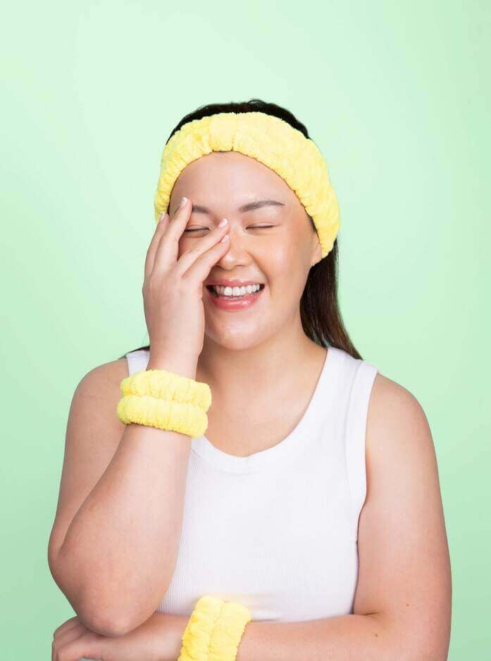Girl laughing wearing yellow skincare headband in turban style and matching yellow face washing arm bands